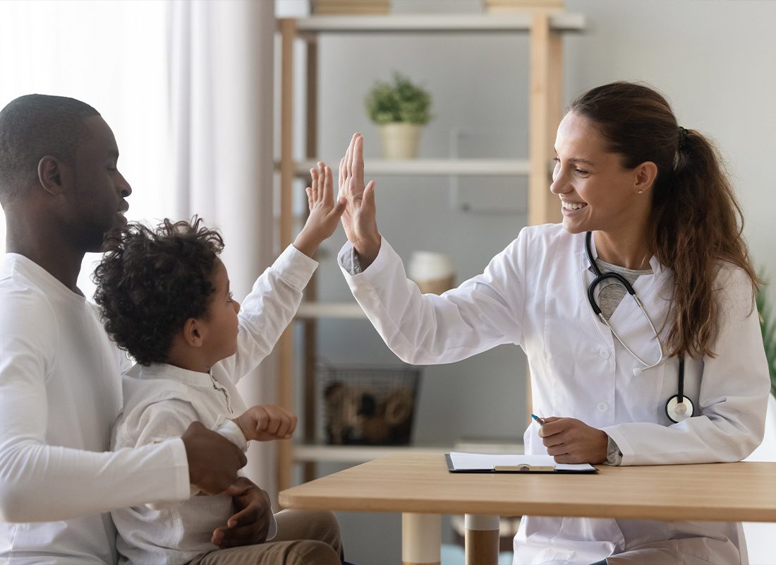 Employee Benefits - Happy Child Giving a Doctor a High Five While on a Doctors Visit With His Dad